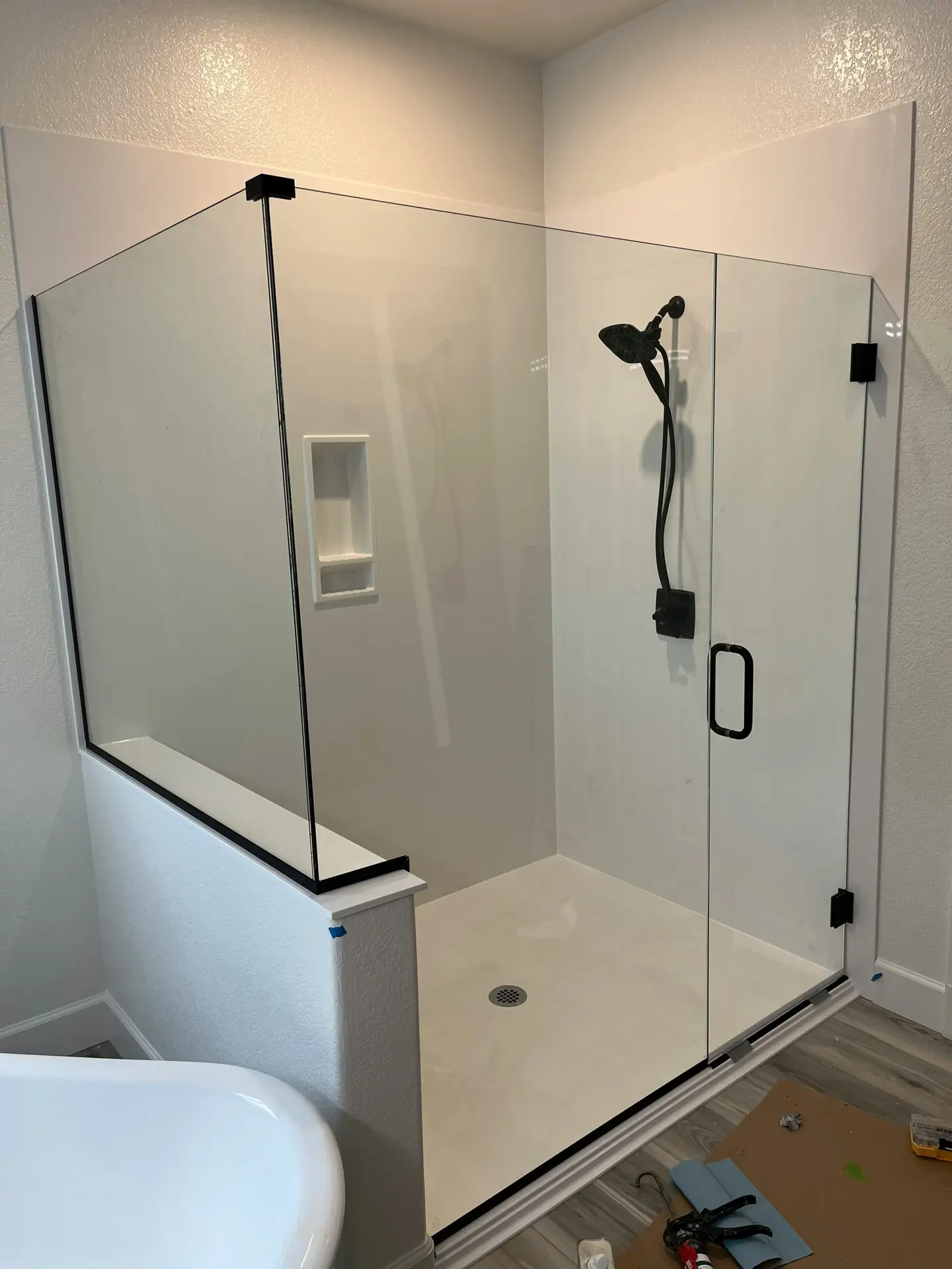 A custom corner walk-in shower renovation in a Vancouver home featuring frameless glass panels, matte black fixtures, and a tiled wall niche.
